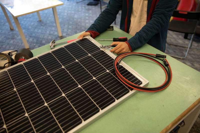 Author working on solar wiring schematic at desk with multimeter and panels in background